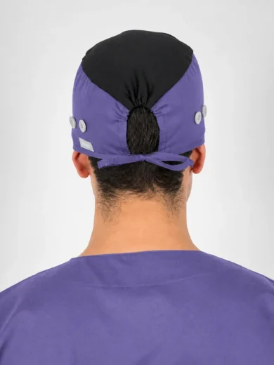 Back view of a person in purple scrubs and a purple surgical cap with a black top, tied at the nape.