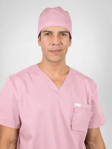 Male healthcare professional in pink scrubs and cap facing the camera with a neutral smile