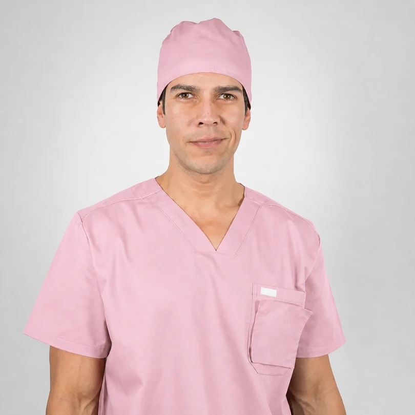 Male healthcare professional in pink scrubs and cap facing the camera with a neutral smile