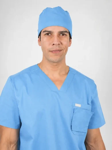 Male healthcare worker in blue scrubs and a surgical cap, smiling at the camera.