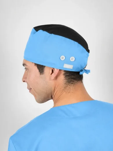 Side profile of a man in blue scrubs wearing a blue surgical cap with a black top and back tie.