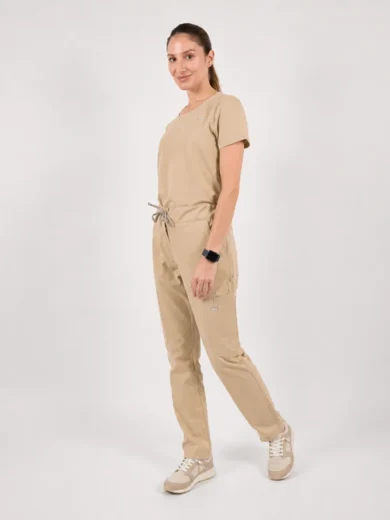 Full-body shot of a woman standing in beige scrubs with a drawstring waist, smiling at the camera.
