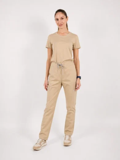 Woman standing in beige loungewear with drawstring pants and sneakers, facing the camera.”