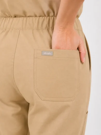 Beige elastic-waist pants with a back pocket; a hand rests in the pocket and a small brand label sits on the pocket’s edge.