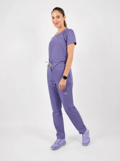 woman in lavender scrubs standing and smiling, with a tied waist and smartwatch on her left wrist