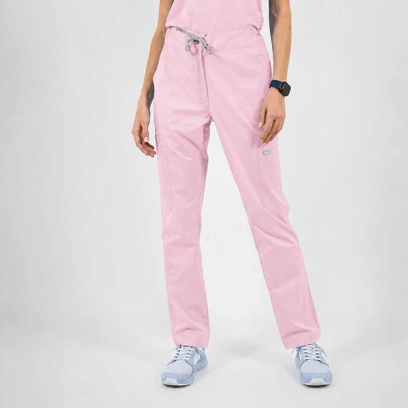 Full-length view of light pink scrub pants with a gray drawstring and front pockets, worn with light blue sneakers and a dark wristwatch.