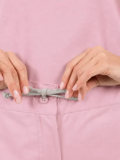 Person adjusts a gray drawstring at the waist of a pink outfit, showing the tied knot and button detail.
