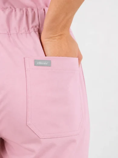 Close-up of a person placing their hand in the back pocket of pink pants, with a small gray brand label above the pocket.