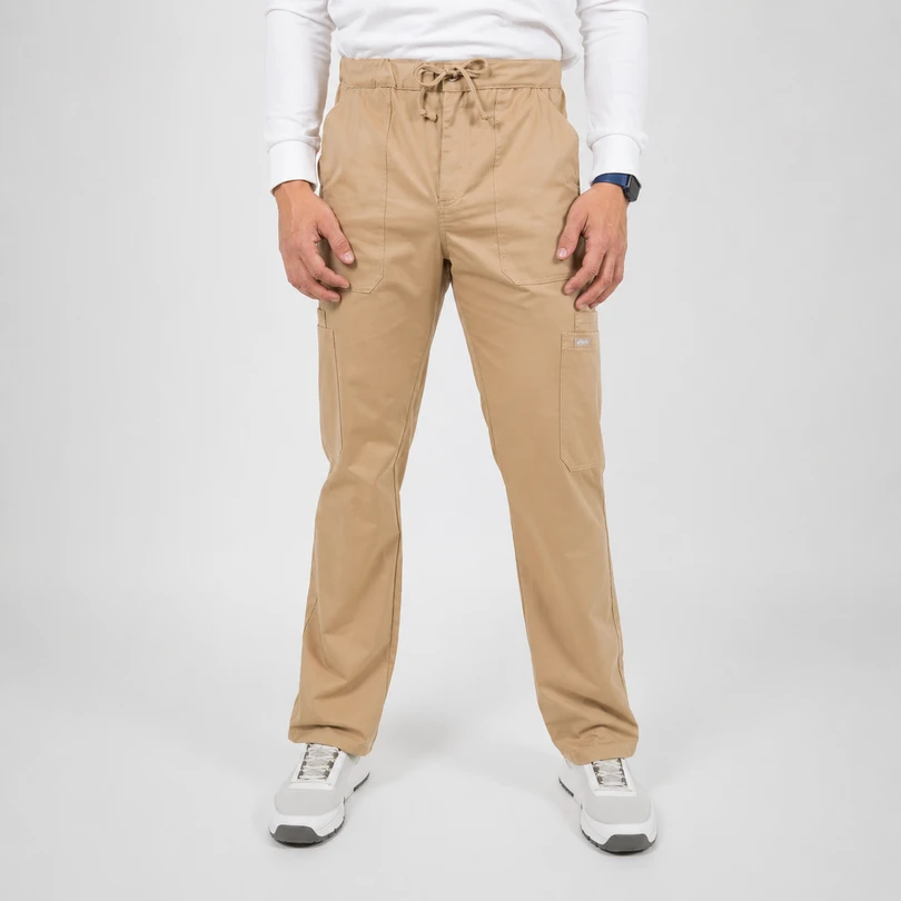 Man wearing tan cargo pants with a drawstring waist, white long-sleeve shirt, and white sneakers, standing against a neutral backdrop.